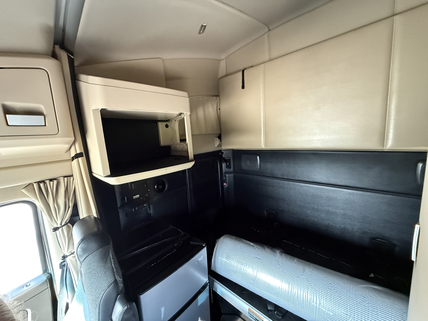 Kenworth T680 sleeper truck interior showing storage compartments and cabinetry with beige upper panels and black lower panels.