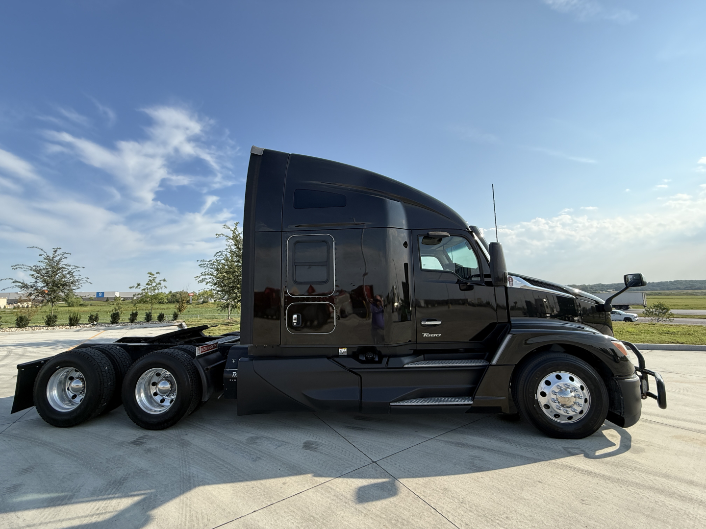 Kenworth T680 semi-truck in black paint, side view showing sleeper cab and triple-axle rear wheels with chrome rims.