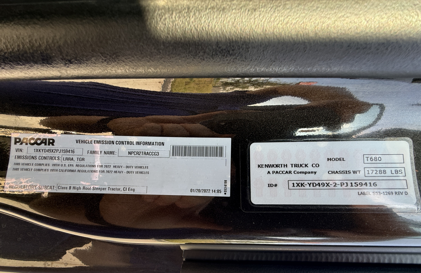 Label stickers on Kenworth T680 showing PACCAR Vehicle Emission Control Information and VIN/stock details. Visible text includes: VIN 1XKYD49X2PJ159416, model 680, chassis wt 17285 lb, ID 1XKYD49X-2-PJ159416.