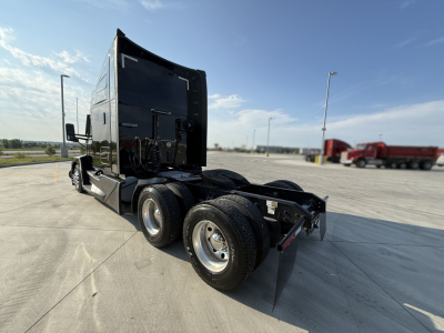 Kenworth T680 tractor 6x4 chassis rear view showing dual rear axles and fifth wheel, black cab with sleeper, concrete lot.