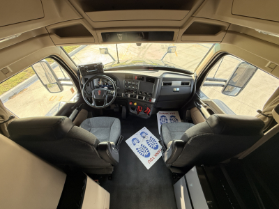 Kenworth T680 interior cab view with dashboard, steering wheel, and driver and passenger seats. Visible are overhead panels, large windshield, side mirrors, and floor mats. No legible text visible.