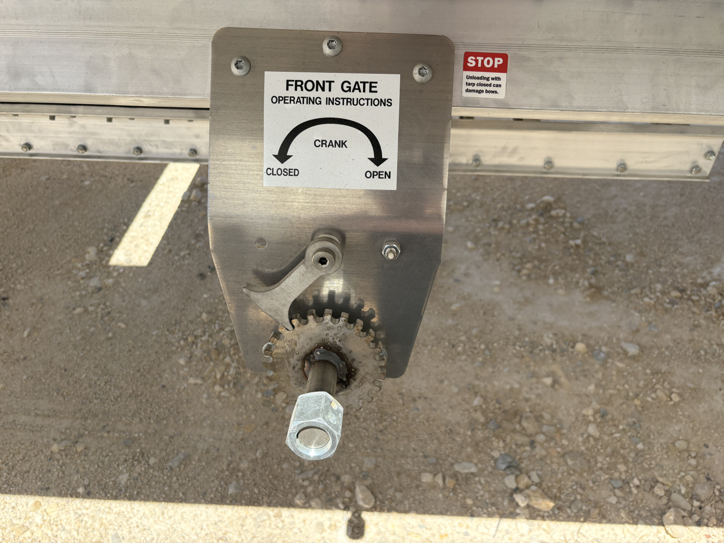 Grain hopper trailer hitch showing front gate crank operating instructions plate and a gear handle.