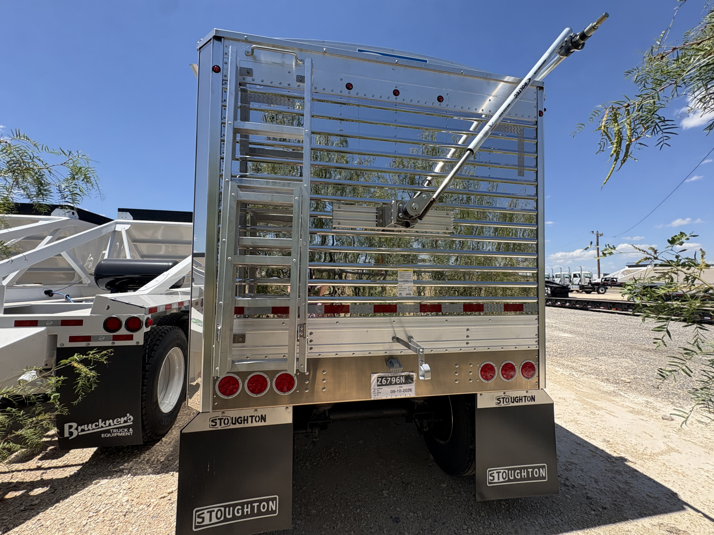 Stoughton 42' aluminum grain hopper trailer rear view with corrugated sidewalls and rear gate, Stoughton branding on mud flaps, license plate area, gravel lot.