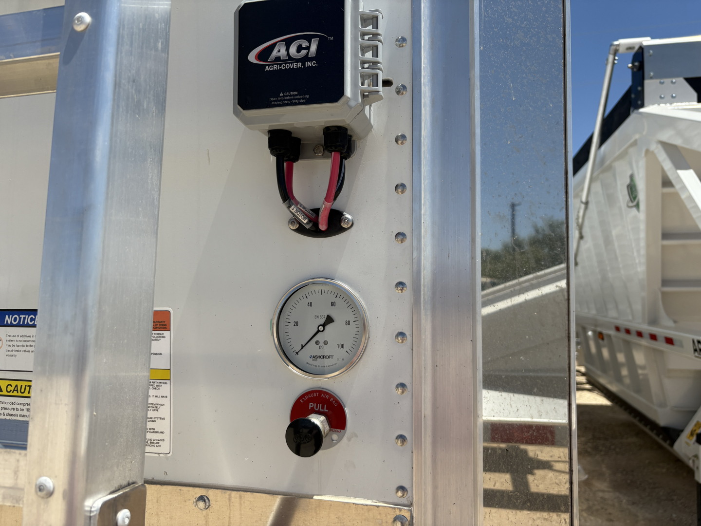 Aluminum grain hopper trailer exterior showing ACF control box, pressure gauge, and pull knob on white panel; 74" corrugated sidewall grain trailer interior visible.