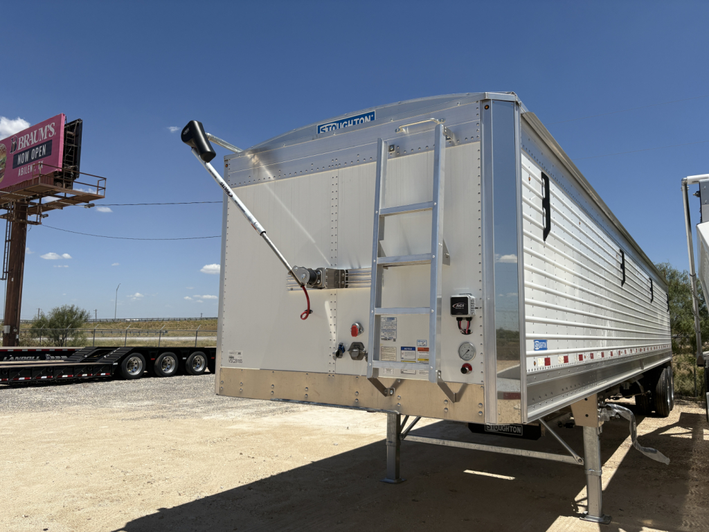 Stoughton 42' aluminum grain hopper trailer with corrugated sidewalls and ladder, rear swing hatch, and landing gear visible.
