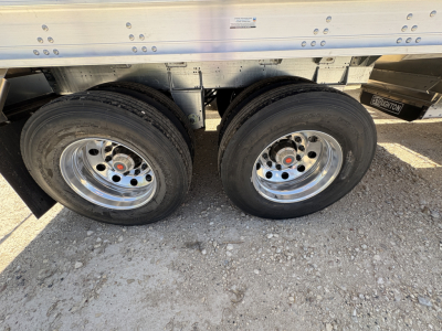 Twin axle trailer wheels with Stoughton logo visible on the frame; sidewall riveted aluminum with 74" corrugated sides; part of a 42' aluminum grain hopper trailer.