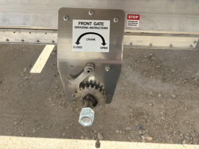Grain hopper trailer hitch showing front gate crank operating instructions plate and a gear handle.