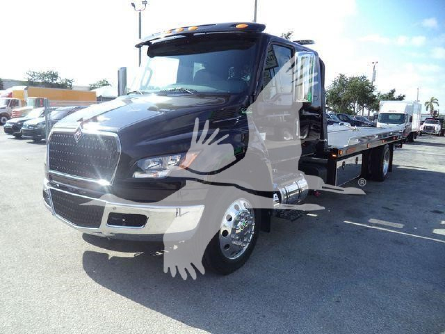 International MV rollback truck with a black body and flatbed, front view showing chrome grille and cab interior.