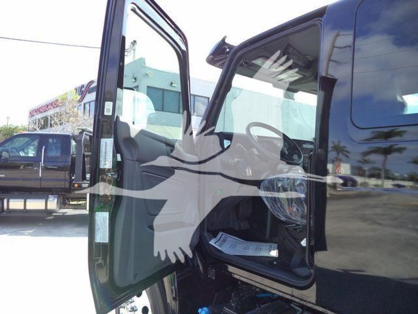 Truck cab interior visible through open driver door showing steering wheel and dashboard; exterior side mirror and open door; reflection of surrounding area.