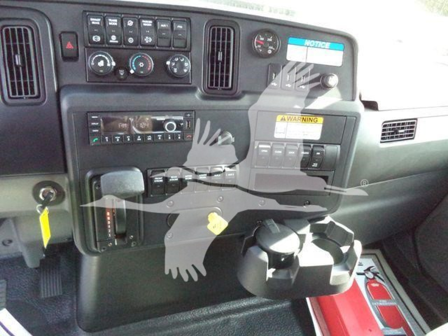 Truck dash cluster showing radio, climate controls, and cup holders; dashboard includes warning labels and various switches; reflection of scissors watermark overlay.