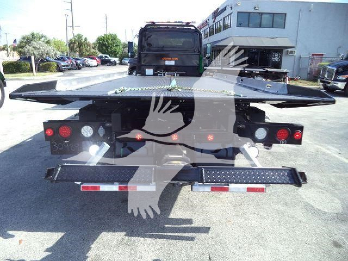 Flatbed rollback truck bed with black metal platform and taillights, view from rear showing load bed and bumper with reflective tape.