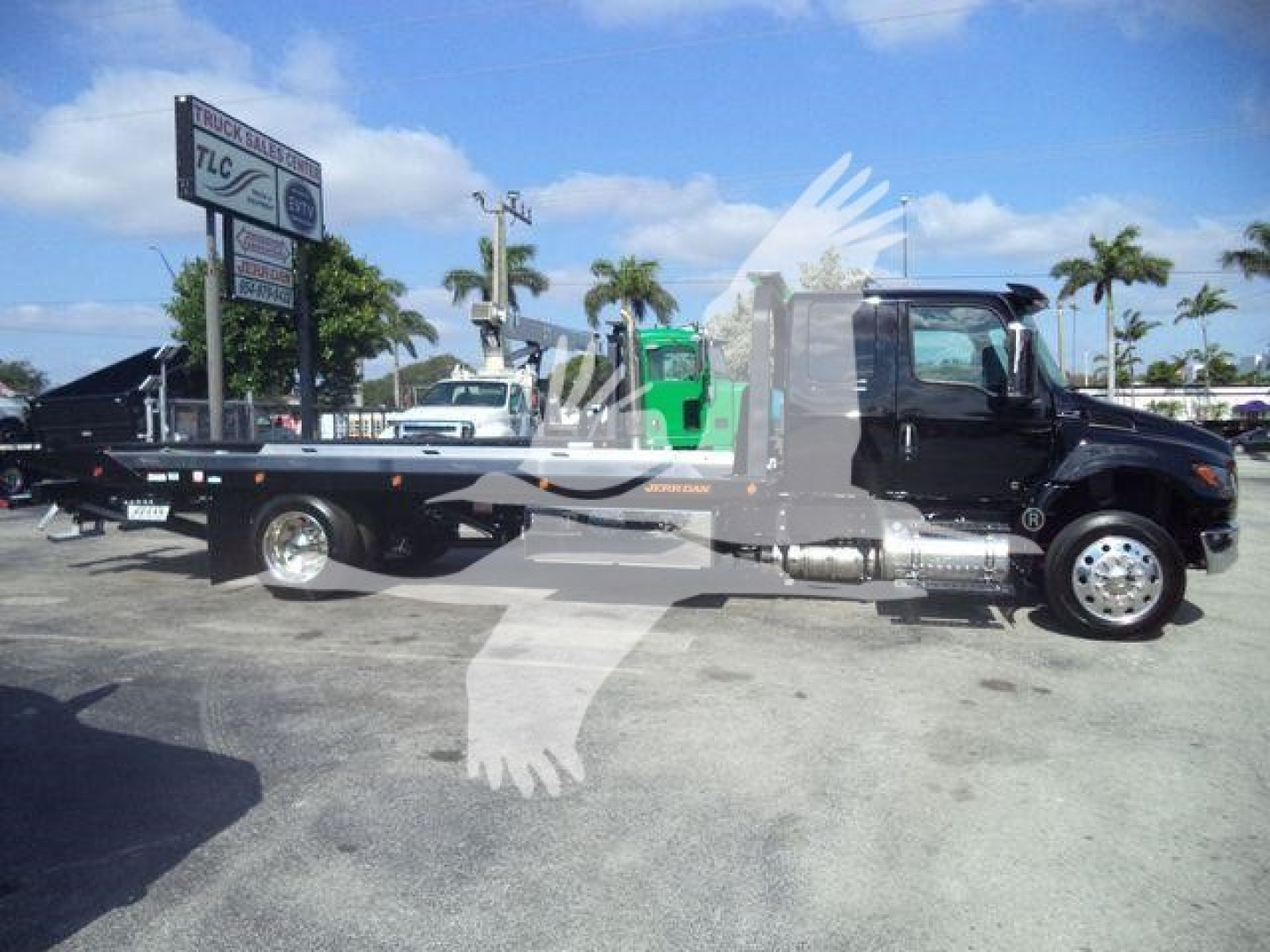 Flatbed tow truck shown in profile with black cab and long flatbed, International MV label not visible.