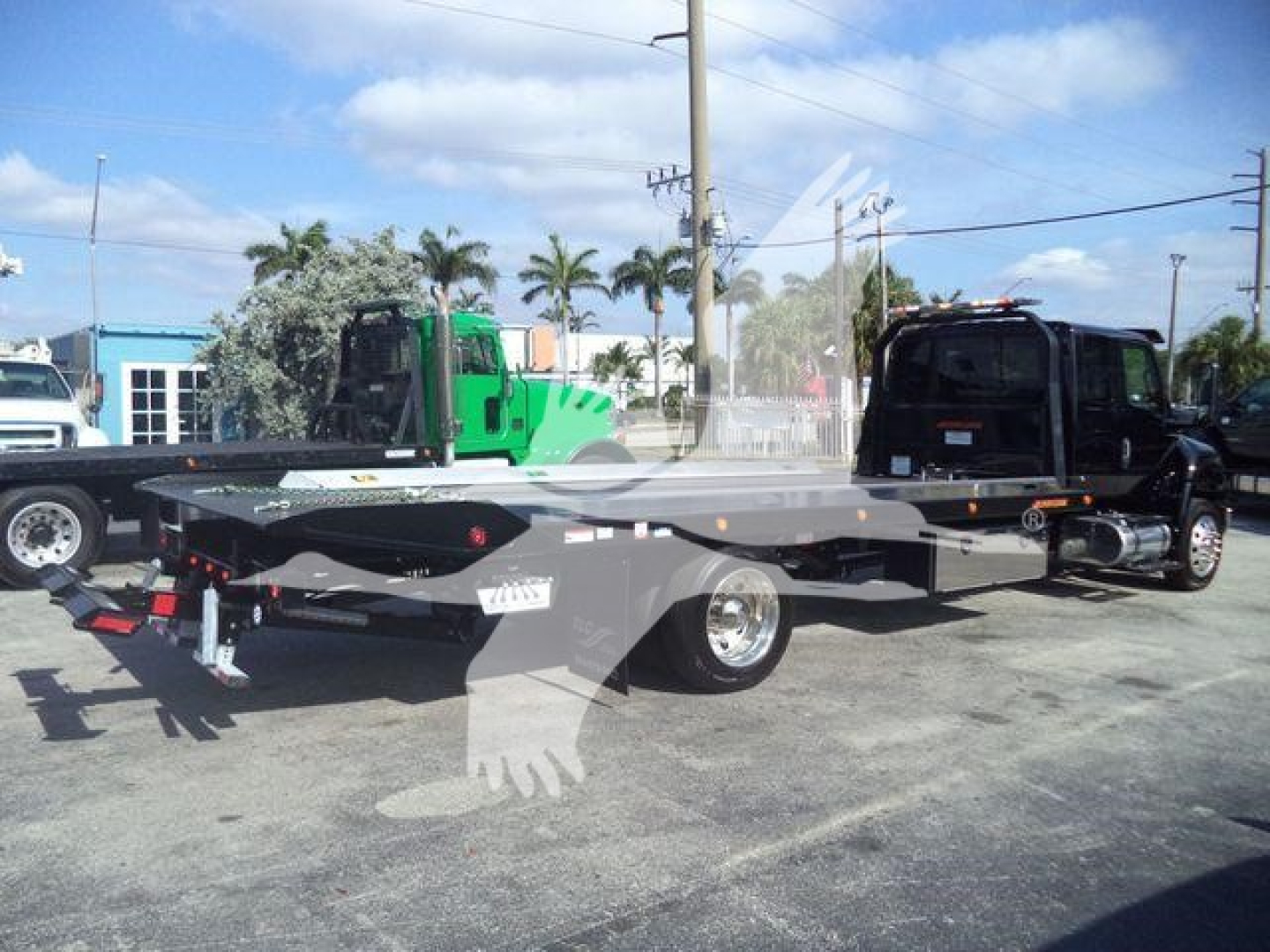 Flatbed tow truck tractor with black cab and long lowbed showing hydraulic controls and reflective markers.