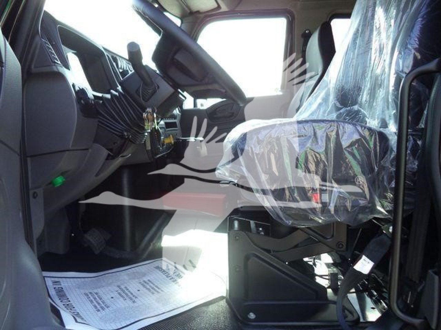 Interior of a new 2027 International MV truck cab showing steering wheel, dashboard, and plastic-covered driver seat. View from open passenger door.