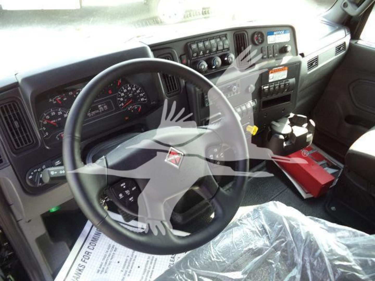 Truck interior dashboard and steering wheel of a new 2027 International MV, with visible gauges, controls, and a red tool/parts case near the center console.
