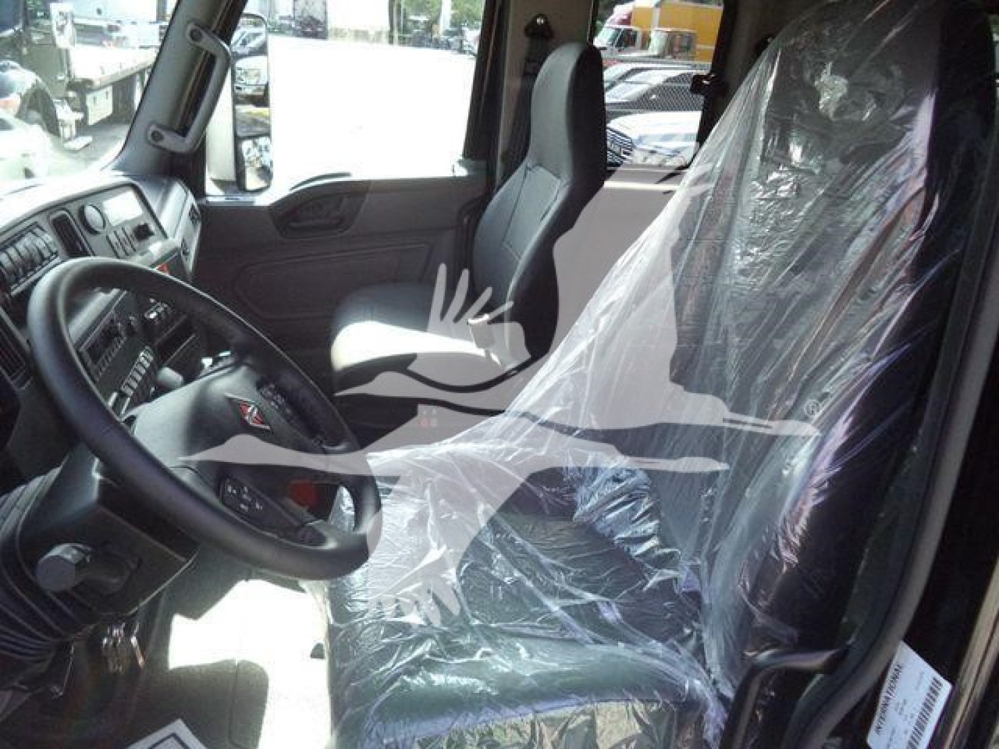 Cab interior of a new 2027 International MV truck showing steering wheel, driver seat wrapped in plastic, and dashboard visible.
