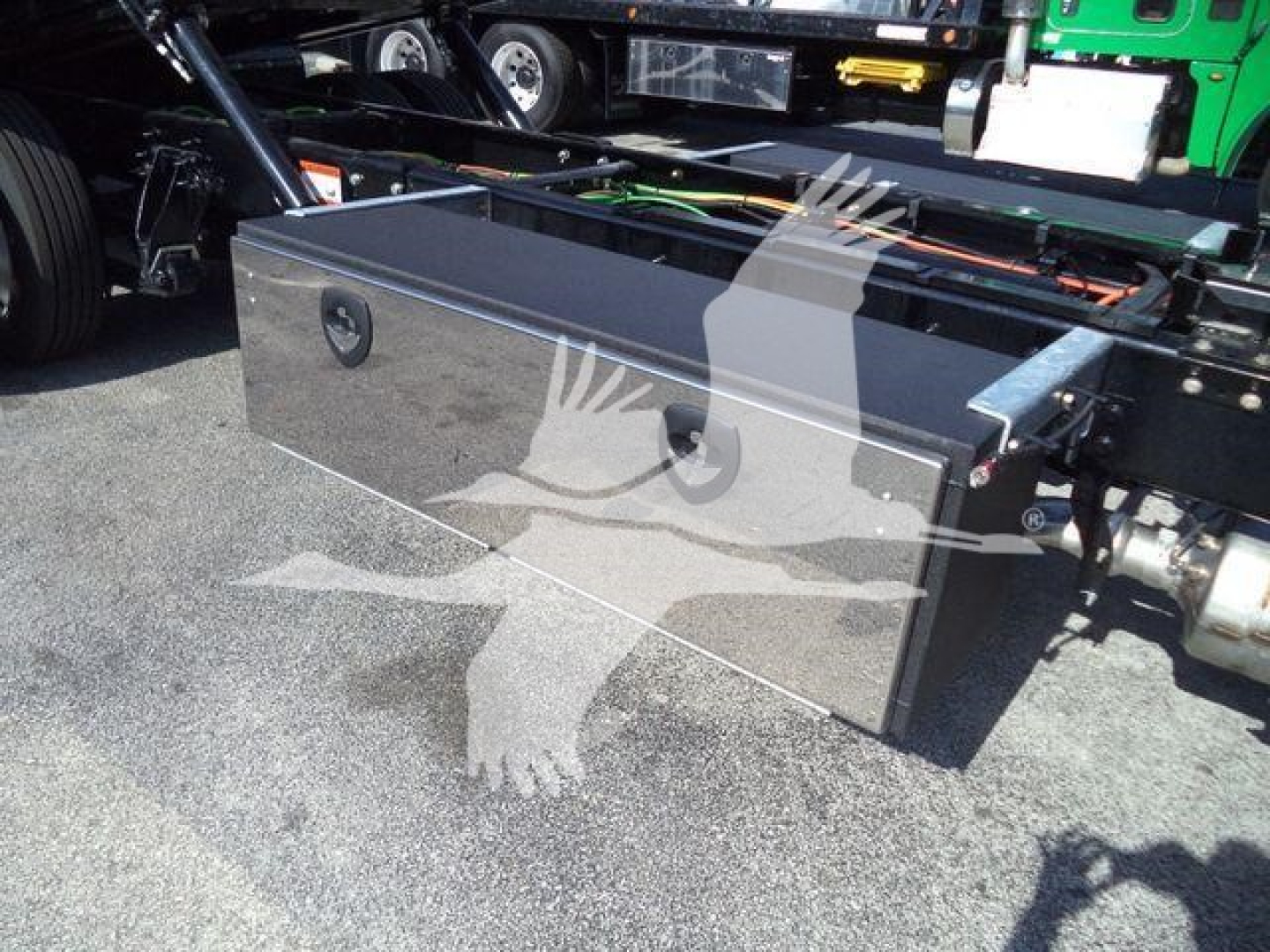 Aluminum toolbox mounted on the chassis of a heavy truck, showing a rectangular metal storage box with two circular lock handles and mounting hardware on a truck frame.