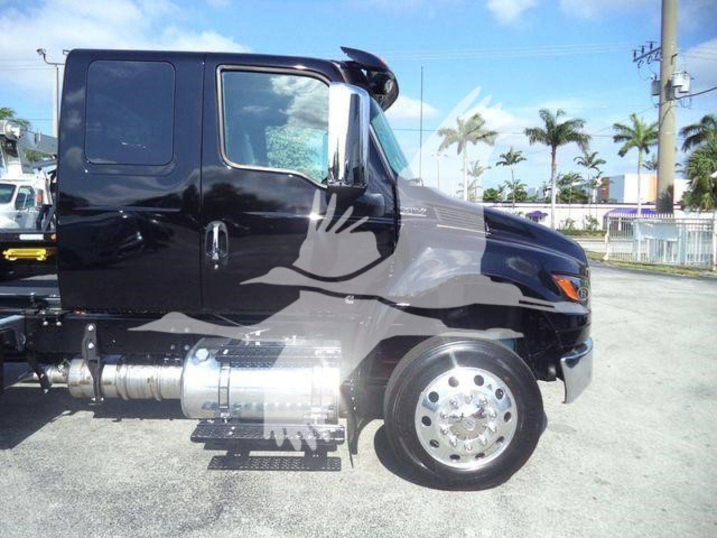 Truck cab with black paint and chrome fuel tanks showing side view of International MV cab and wheel assembly.
