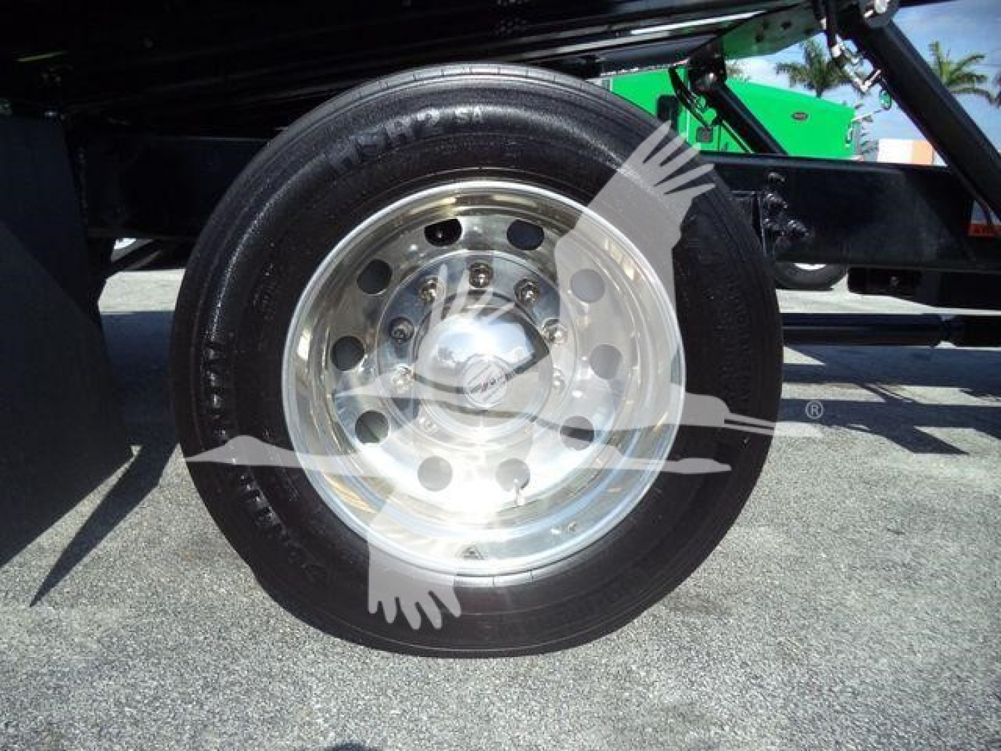 Wheel and tire on truck chassis showing a polished steel rim and tire sidewall with minimal text visible.