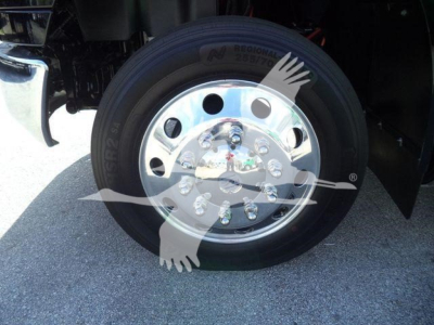Wheel and chrome hub on International MV truck front axle showing polished steel rim, lug nuts, and tire with visible tread.