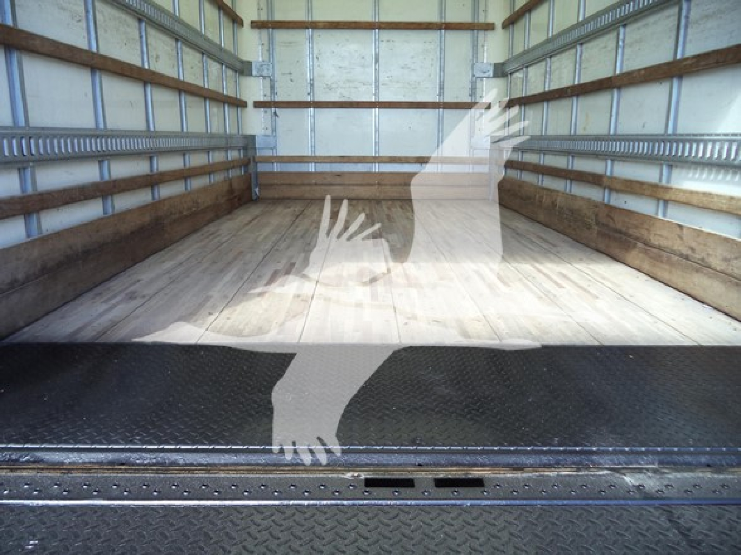 Isuzu NPR HD box truck interior cargo area with wooden floor and metal side rails; empty at rear showing cargo area and ramp edge.