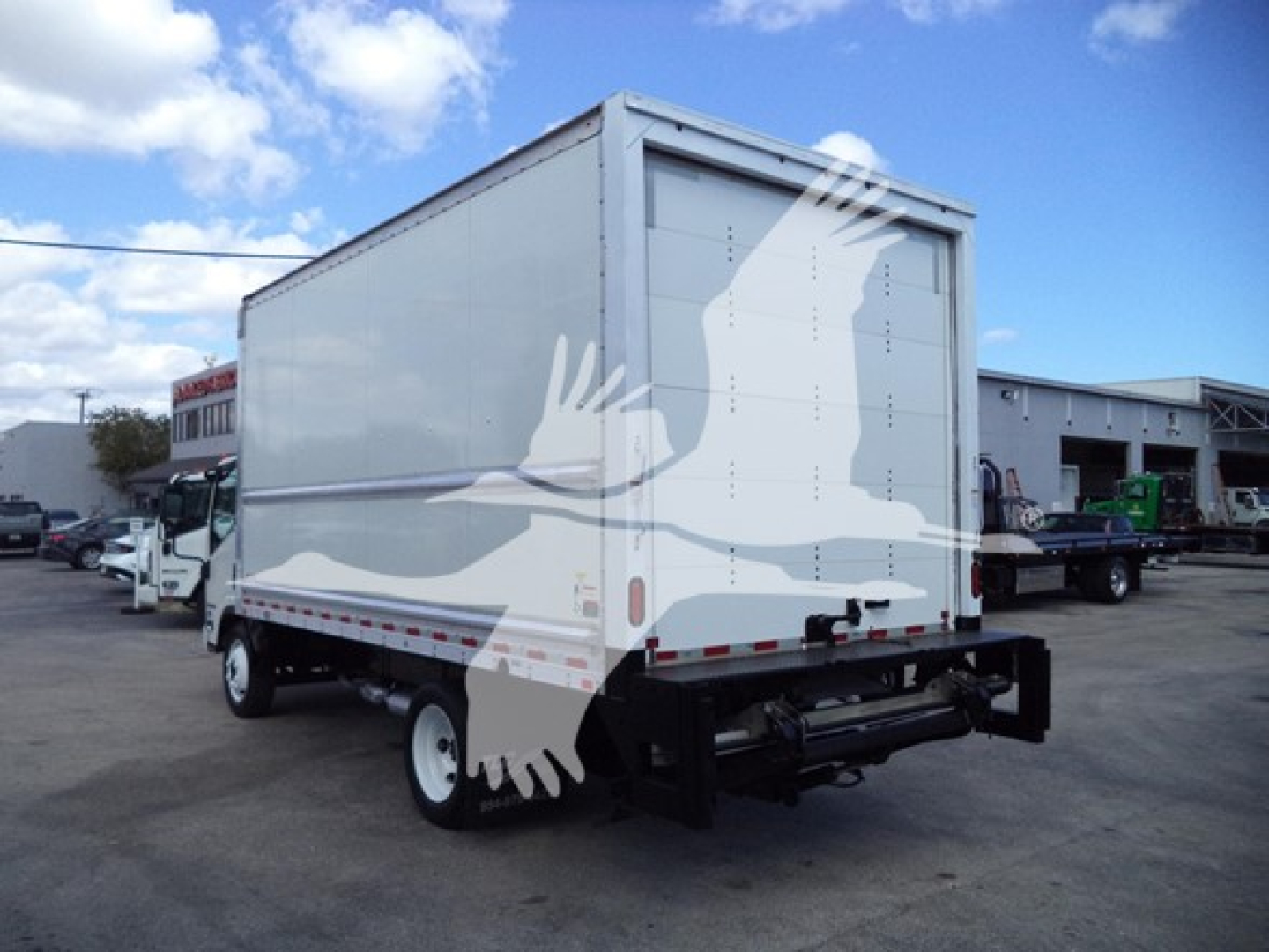 Isuzu NPR HD box truck rear/side view with closed cargo box and bumper hitch in a dealership lot.