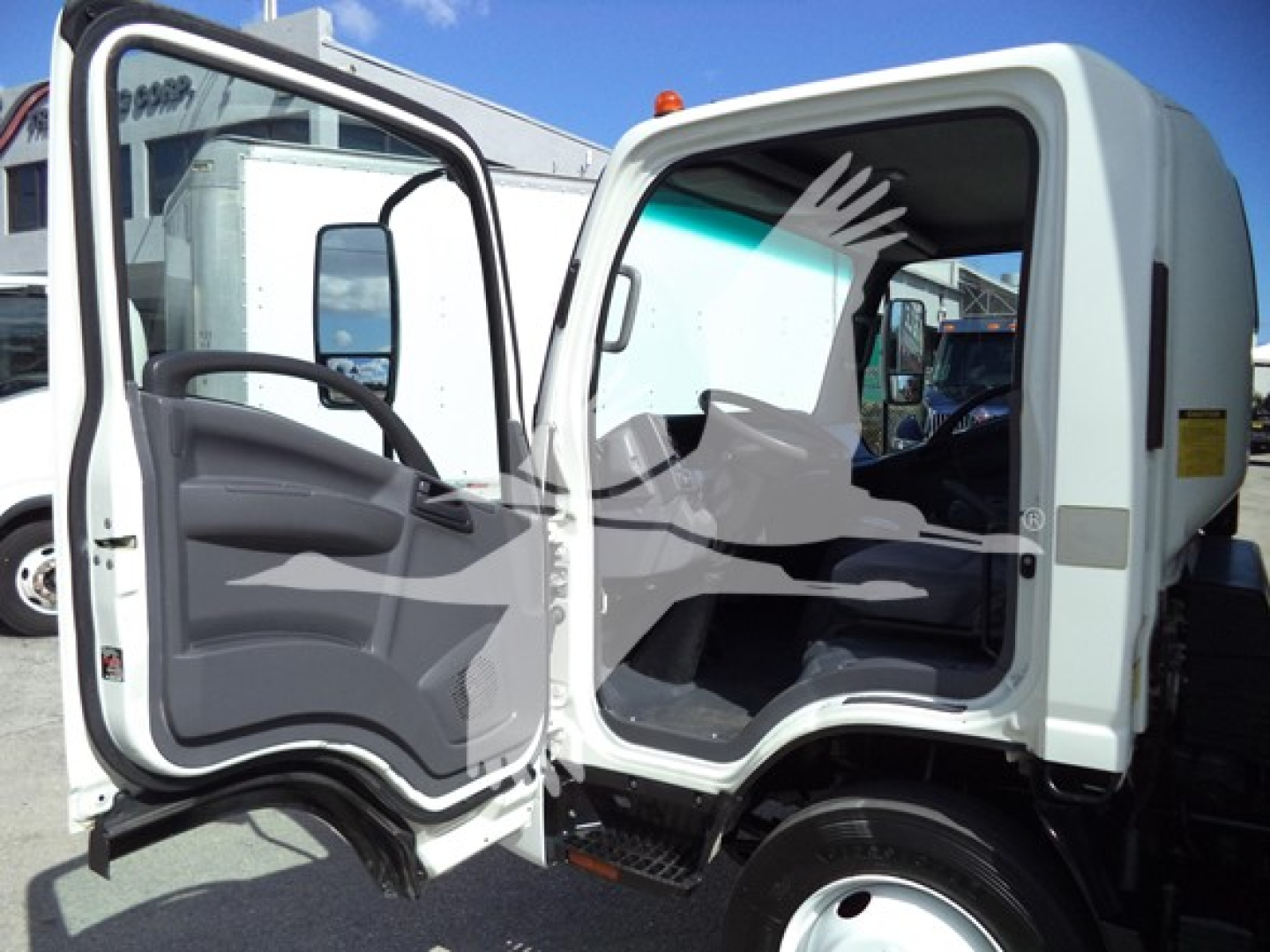 Isuzu NPR-HD cab interior and open door showing driver's seat and dash with cargo area visible, white cab, side step, in-service vehicle.