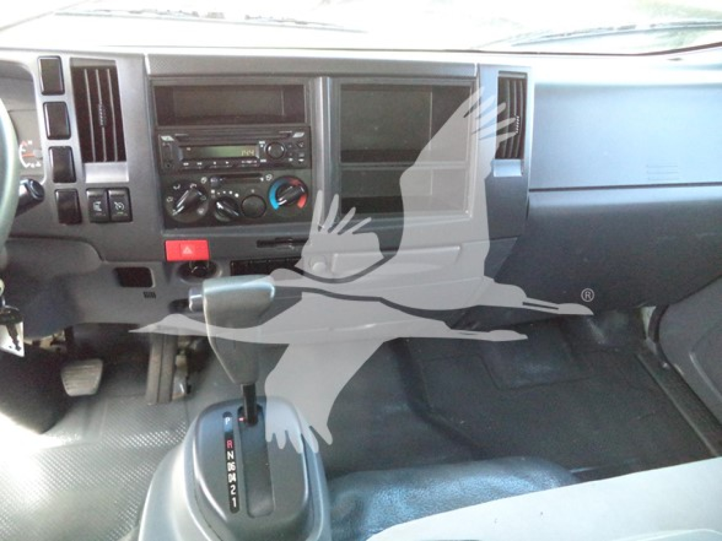 Dashboard area of a 2020 Isuzu NPR HD cargo truck showing center console with radio, climate controls, pedals, and gear shifter.