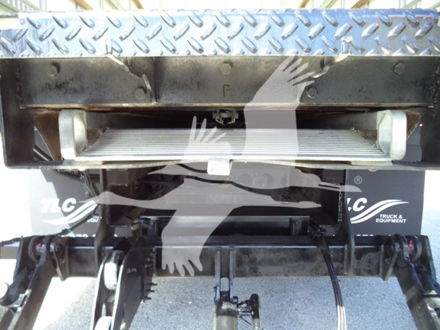Isuzu NPR HD medium-duty truck bed area showing storage/ladder rack and hydraulic lines with diamond plate pattern on top.
