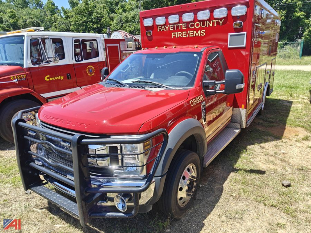 Ford F-450 Super Duty ambulance with red body, front bull bar, 'Fayette County Fire/EMS' on cab, emergency lights, side steps, and raised rear compartment.