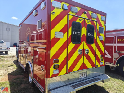 Rear view of a 2019 Ford F450 ambulance with red body and yellow chevron rear, EMS and FIRE labels on doors, license plate visible.