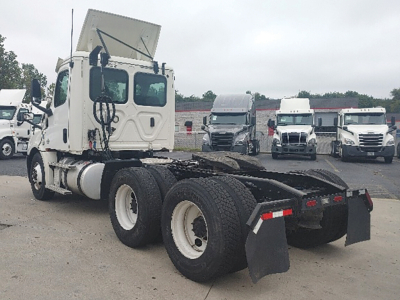 Semi truck tractor’s rear chassis and dual rear axles with mud flaps; white cab with tilt hood visible; other trucks in background.