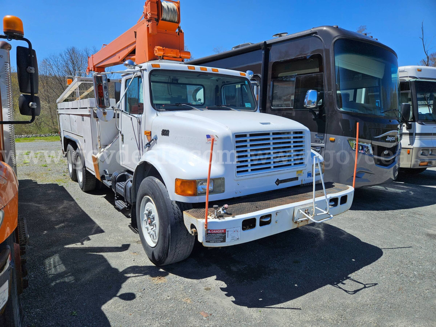 International 4900 truck with boom, front view showing white cab, orange boom on a utility body, large grille, headlights, and front bumper.