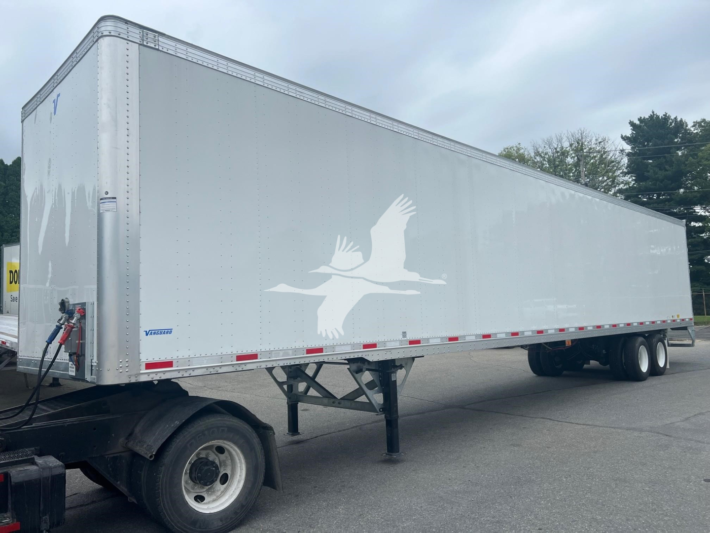 Trailer side view showing a large white logo of a bird in flight on a Vanguard Maxcube trailer with a dual-axle rear in a parking lot.