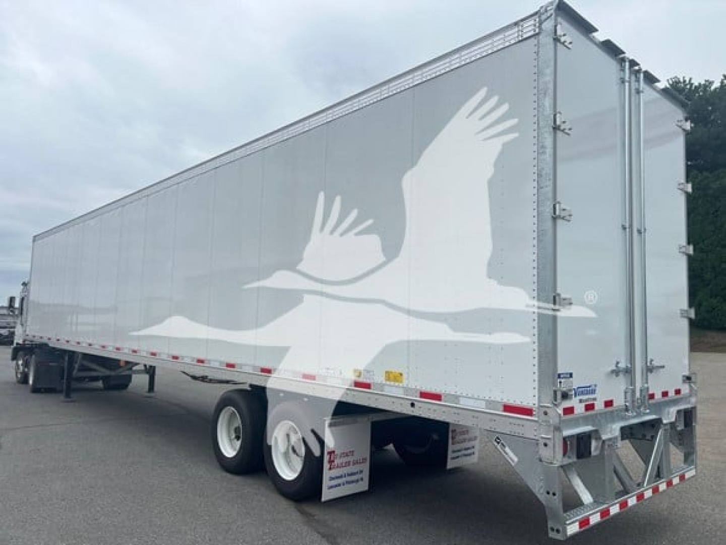 Trailer side showing a large white graphic of birds in flight and a grey aluminum trailer with dual rear doors.