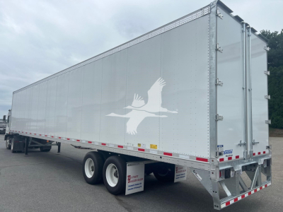 Trailer side view showing Vanguard Maxcube trailer with white exterior and large logo on midsection.