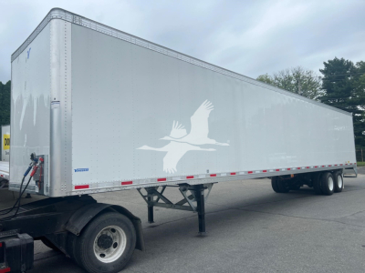 Trailer side view showing a large white logo of a bird in flight on a Vanguard Maxcube trailer with a dual-axle rear in a parking lot.