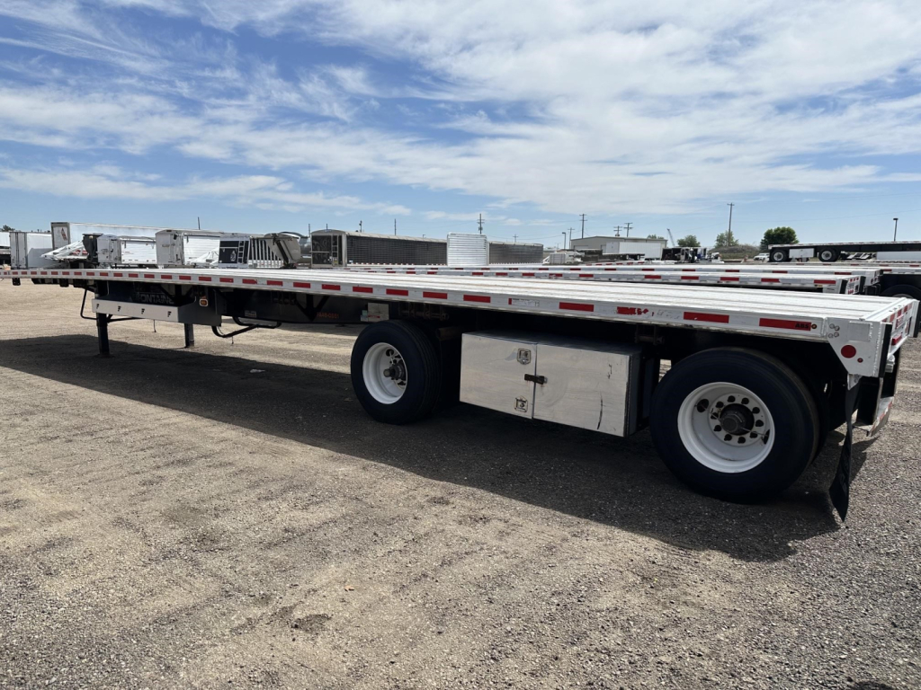 Flatbed trailer side view showing tandem axles and storage/toolbox undercarriage with writable signage panels.
