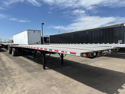 Flatbed trailer with Fontaine spread air combo, aluminum deck, dual rear axles, visible ramps and wheels in a truck yard.
