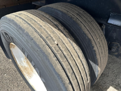 Dual rear trailer tires with weathered tread and rims on a Fontaine spread air combo flatbed trailer; visible bias-ply tread and dirt.