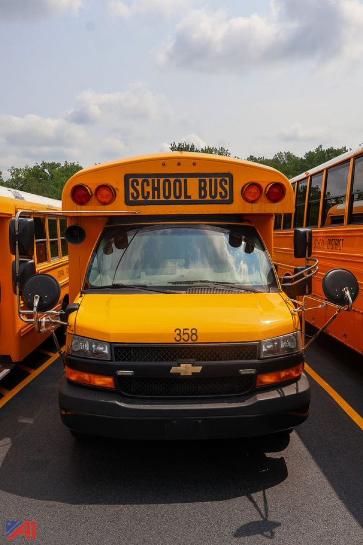 Front view of a yellow 2020 Chevrolet Thomas express mid-size wheelchair school bus with 'SCHOOL BUS' sign and number 358 on hood, flanked by other buses.