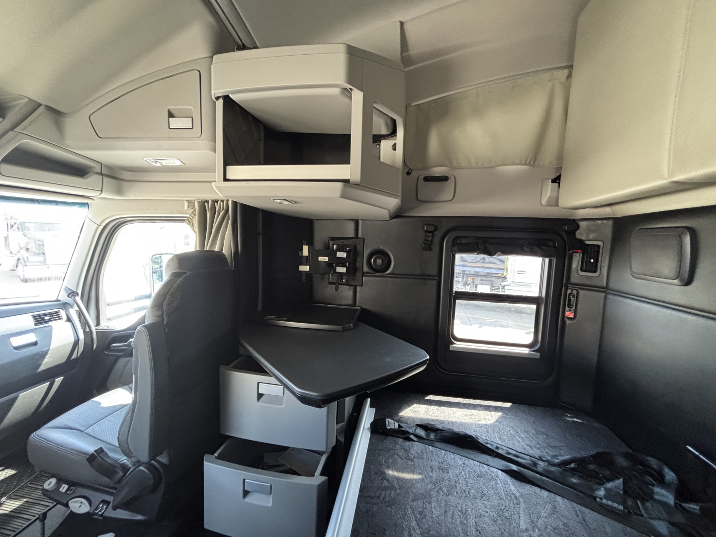 Kenworth T680 cab interior showing bunk area, overhead storage, and mounted desk/table with drawers.