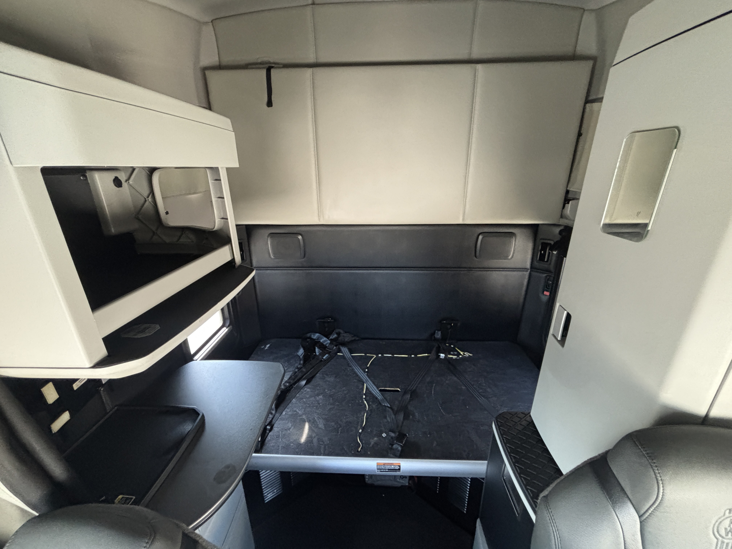 Kenworth T680 sleeper cab interior showing bed area with overhead storage and belts laid out.