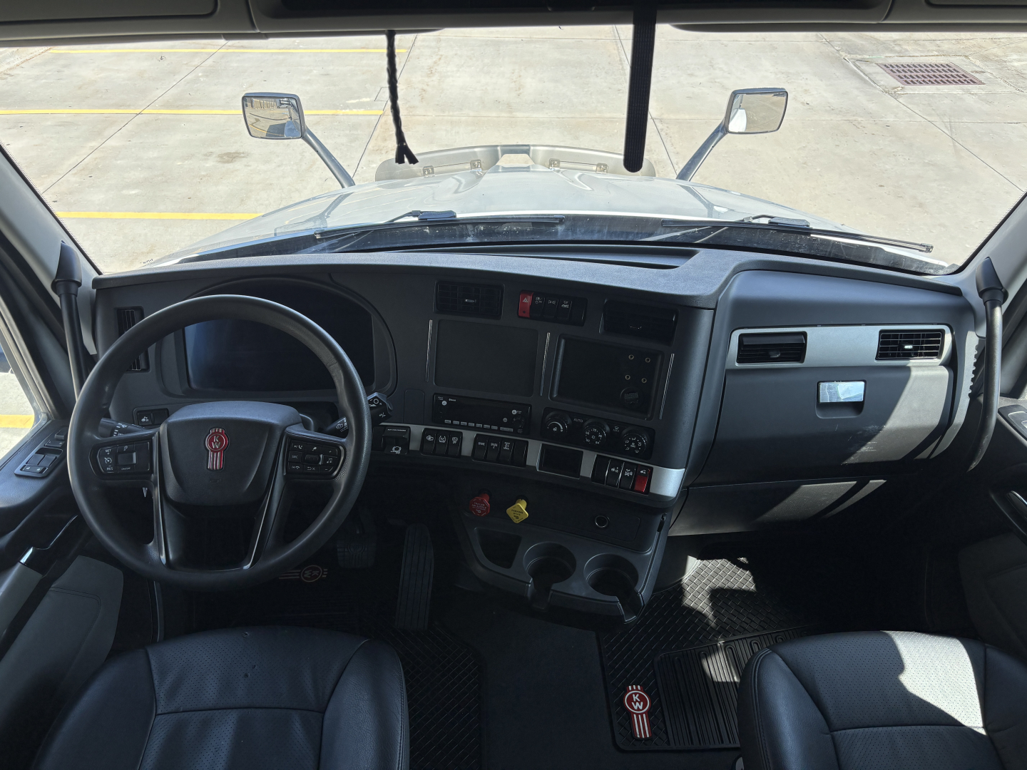Kenworth T680 interior dashboard view from the driver seat showing steering wheel, instrument panel, center console, and windshield. Text on stickers and controls not clearly legible.