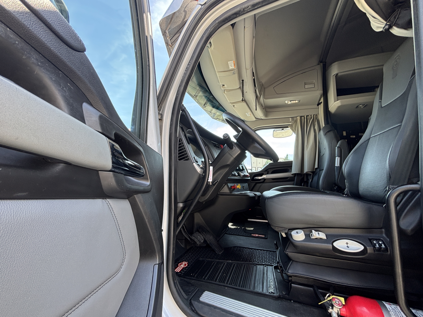 Kenworth T680 truck interior driver side shows cab with steering wheel, seat, control panels, and steps; dashboard and door panels visible.