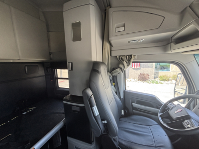 Truck cab interior of a Kenworth T680 with sleeper, showing driver seat, passenger seat, overhead storage, and window. No legible model text visible in image.