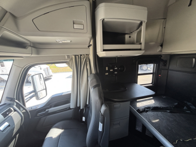 Kenworth T680 interior cab view showing sleeper area, dashboard, and overhead cabinet with a small desk area.