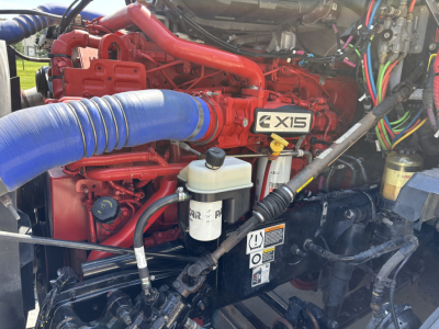 Kenworth T680 engine bay showing X15 badge and red engine with blue intake hose and various wiring and fluid reservoirs.