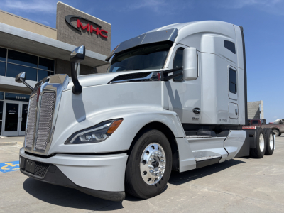 Kenworth T680 conventional sleeper truck in silver/gray outside dealership, showing front grille, large mirrors, and side cab with aerodynamic design.