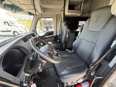 Interior of a 2023 Kenworth T680 cab showing driver seat, steering wheel, dashboard, and passenger seat.